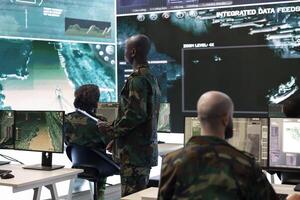 Military personnel undertaking a secret service operation with real time data on a big screen, field troops examining satellite CCTV imagery. Conducting a reconnaissance mission in control center. photo