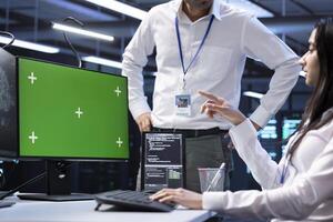Software developers doing checkup on green screen computer in server room used for artificial intelligence workloads. IT staff members inspecting neural network data center facility with mockup PC photo