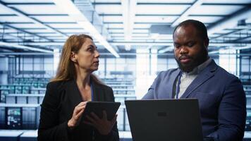 Teamworking technicians managing data center with advanced technology using devices. Coworkers in server room optimizing data center infrastructure with laptop and tablet, camera B photo