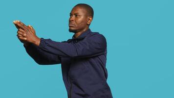 Portrait of security guard overseeing premises to prevent intrusion pretending to shoot gun. Private law enforcement worker doing pistol fingers hand gesture, studio backdrop, camera A photo