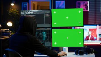 Hooded man writing lines of code on green screen PC from apartment, trying to get past security systems. Evil hacker using mockup computer to make scripts that can hack devices, camera A photo
