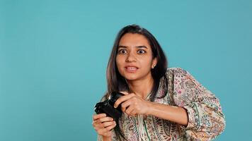Jolly gamer celebrating after winning game on gaming console, studio background. Delighted Indian woman bragging after being victorious in videogame, defeating all enemies using gamepad, camera B photo