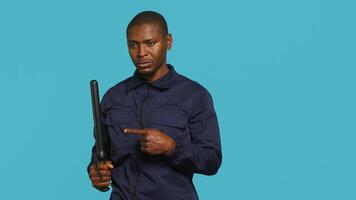 Security guard removing baton from belt, preparing to attack suspects. Portrait of bodyguard pointing finger towards truncheon, threatening to subdue criminals, studio background, camera A photo