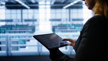 System administrator doing annual checkup using tablet to prolong data center equipment life span. Close up shot of IT expert in server hub monitoring supercomputers using digital device, camera B photo