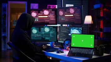 Hacker doing computer sabotage using trojan ransomware on green screen laptop. Cybercriminal uses mockup device to demand ransom money from victims in exchange for access to their data, camera B photo