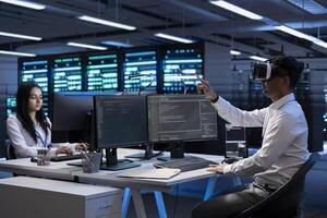Team of engineers immersed in virtual reality in server farm, doing units maintenance. IT experts coworkers using VR headset to optimize servers performance, checking operations in data center photo
