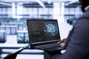 System administrator in data center using laptop to visualize artificial intelligence neural networks made up of interconnected nodes. Close up of employee oversees AI systems processing information photo