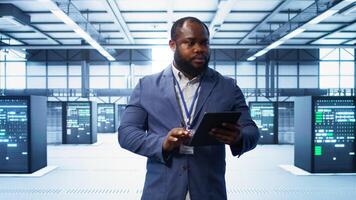 IT technician walking in data center, overseeing server operations using tablet. Expert ensuring optimal performance and data integrity in server hub using digital device, camera B photo