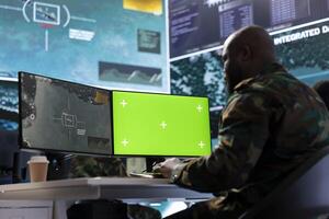 Military specialist monitors satellite data next to green screen display, working at command post with high tech gear to support important army defense operations. Coordinates strategic missions. photo