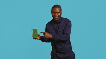 Portrait of upbeat security staff member showing green screen smartphone. Cheerful patrolling agent maintains secure environment, showcasing mockup phone, studio background, camera B photo