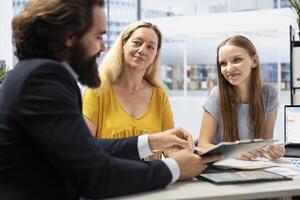 Financial advisor creating reports on investment performance, showing them to mother and daughter. Agent in office presenting portfolio economic evolution to family members photo