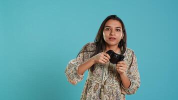 Focused woman playing videogames with motion controlled joystick, studio background. Indian gamer participating in online multiplayer racing game using gyroscope function on gamepad, camera A photo