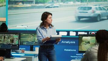 Manager overseeing employees in monitoring traffic activity, operating through surveillance footage on CCTV cameras. Diverse team work with satellite system in control center. Camera A. photo