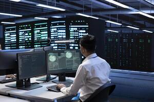 System administrator using computer in server room to support global connections using their hardware. Employee inspecting data center equipment supporting worldwide network using PC photo