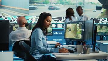 Indian woman operator locating delivery truck and offers gps coordinates of the shipment location. Control center employee consults satellite map and CCTV system for routes. Camera B. photo