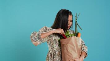Upset woman frowning after forgetting to buy everything, looking inside paper bag with vegetables. Conscious living person sulking after realizing some groceries are missing, camera A photo