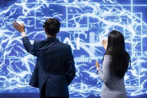 Engineer wearing VR headset looking at hologram of artificial intelligence human brain simulation, assisted by colleague. IT specialist and coworker interacting with AI visualization photo
