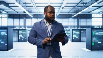 IT technician walking in data center, overseeing server operations using tablet. Expert ensuring optimal performance and data integrity in server hub using digital device, camera B photo