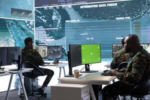 Soldier gathering real time surveillance data next to mockup display in high tech command center, processing intelligence for field troops operations. Working with modern gear and big screen. photo