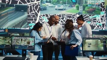 Diverse employees group discussing ways to speed up order delivery, looking for routes to avoid traffic on satellite navigation. Agency operators use CCTV footage in monitoring room. Camera B. photo