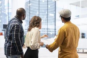 Real estate agent and clients discussing detailed blueprints for a new office property, evaluating the architectural design and layout in a modern high class building. Investment opportunity. photo