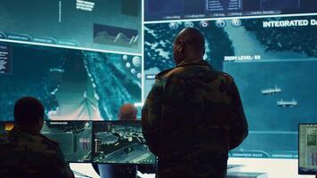Commander and his crew operating radar systems via CCTV and satellite to detect and track enemy aircraft or missiles. Military officer uses big screen in control center to guarantee safety. Camera A. photo