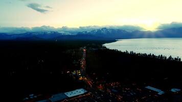 View from a height of the evening city near the sea on the horizon of snow-capped mountains and fluffy clouds. Lanterns burn brightly, the road is illuminated by car lights. Slow traffic on the roads video