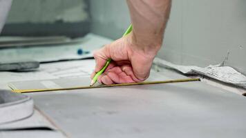 A close-up craftsman crosses the tile with a pencil for correct laying of the tile. video
