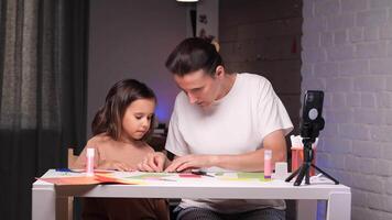 mom teaches her daughter to make a paper craft using an online lesson on phone video