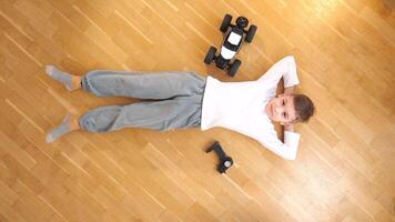top view of a boy lying on his back on the floor, model of rc car stands nearby video