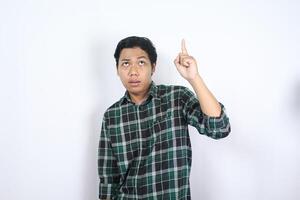 puzzled young asian man pointing above and looking up with wondering face and clueless expression isolated on white background photo