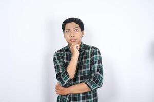 portrait of curious asian young man wearing casual clothes looking above with hand on chin thinking isolated on white background photo
