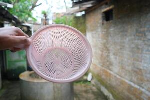 A pink plastic colander held up in a hand in front of a stone wall. photo