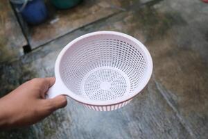 Close up of a hand holding a white plastic colander. photo
