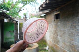 Close-up of a pink plastic strainer held in hand, blurred background of a stone wall and greenery. photo