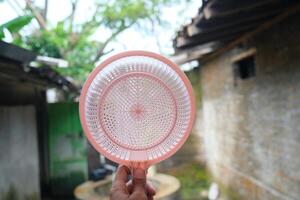 A hand holds a pink plastic strainer in front of a blurry background. photo