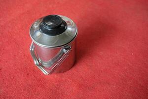 A silver pitcher with a black lid on a red surface. photo