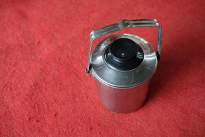 Silver thermos with black top and handle on red background. photo