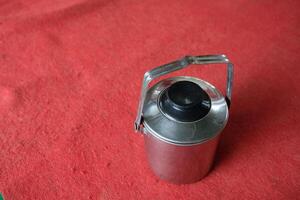 Silver thermos with a black lid on a red surface. photo
