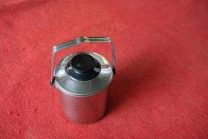 A stainless steel thermos with a black lid and handle on a red surface. photo