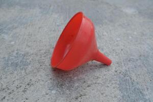 Red plastic funnel lying on a gray concrete surface. photo