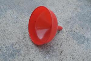 Red plastic funnel lying on a concrete surface. photo