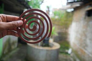 Close-up of a brown mosquito coil held in a hand, with a blurred background of an outdoor setting. photo