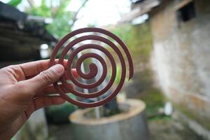 Closeup of a hand holding a brown mosquito coil, blurred background. photo
