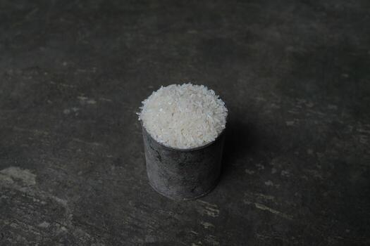 White rice in a rustic metal container on a textured grey surface. photo