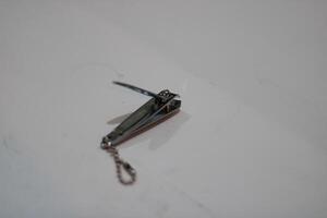 A close-up of a silver nail clipper with a chain. photo