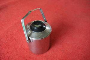 Silver thermos with a black lid on a red surface. photo