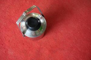 Top view of a silver metal container with a black lid and handle on a red surface. photo