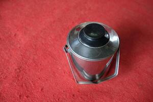 Stainless steel container with black lid on red surface. photo