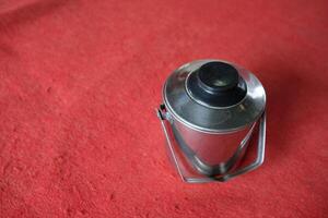 A silver container with a black lid sits on a red surface. photo